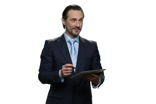 Smiling businessman is writing on the tablet. Successful well-dressed man with pen isolated on white wall.