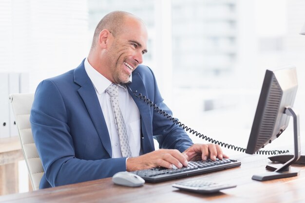 Smiling businessman on the phone and using his computer