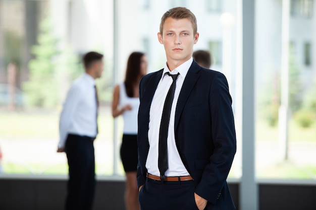 Smiling Businessman posing while colleagues talking together in office.