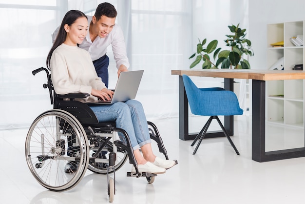 Uomo d'affari sorridente che mostra qualcosa alla sua giovane donna disabile sul computer portatile nell'ufficio