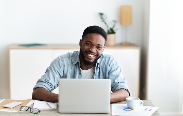 Smiling businessman sitting at workplace in modern office and laughing