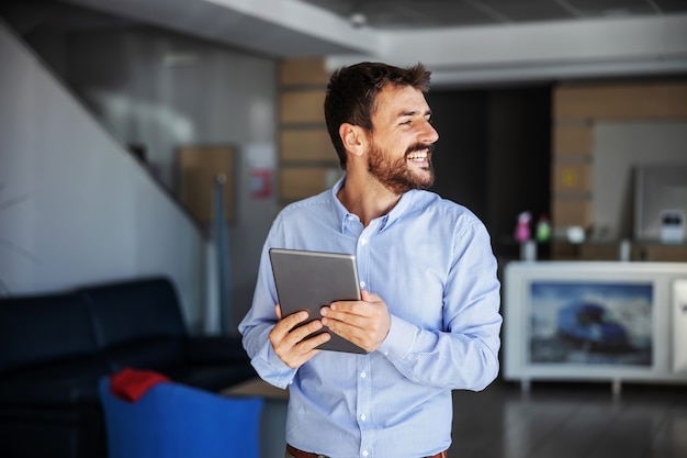 Uomo d'affari sorridente in piedi nella hall della ditta di esportazione e utilizzando tablet.