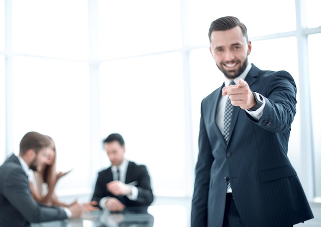 Smiling businessman standing in the office and pointing at youphoto with copy space