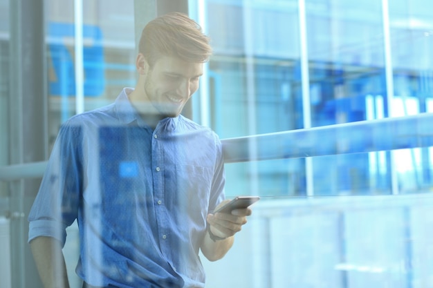 Smiling businessman standing and using mobile phone in office.