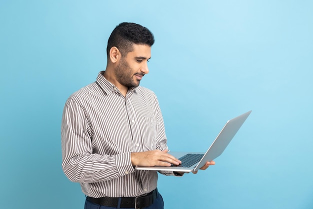 Smiling businessman standing with portable computer in hand looking at display typing on keyboard