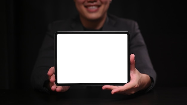 Smiling businessman in suit showing digital table with blank screen