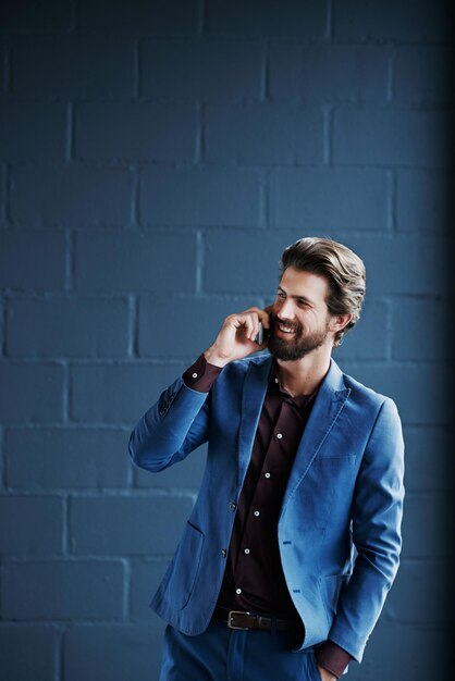 Smiling businessman talking on phone against wall