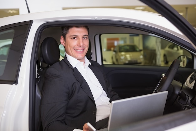 Uomo d'affari sorridente che utilizza computer portatile nella sua automobile