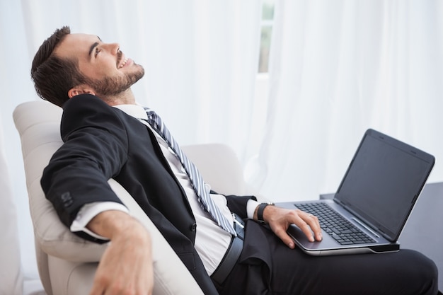 Smiling businessman using laptop on his couch