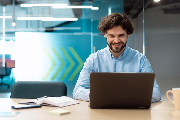 Smiling businessman using laptop sitting at desk in office