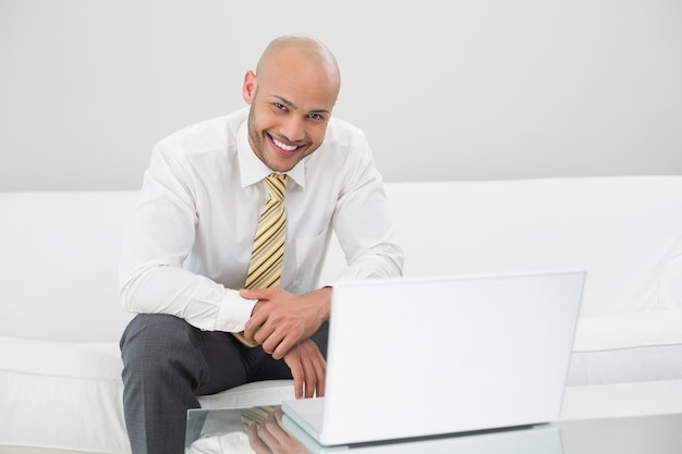 Smiling businessman using laptop on sofa at home