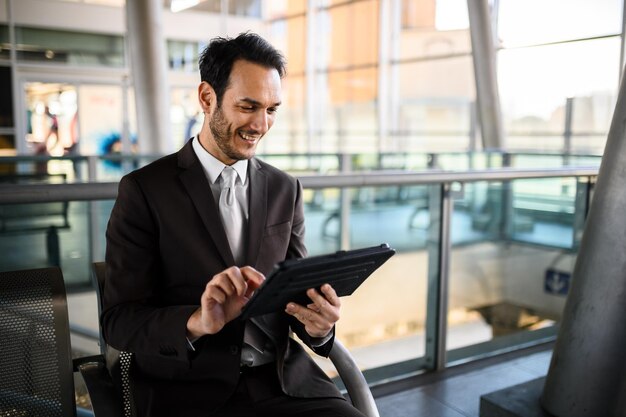 Foto uomo d'affari sorridente che usa il tablet all'aeroporto