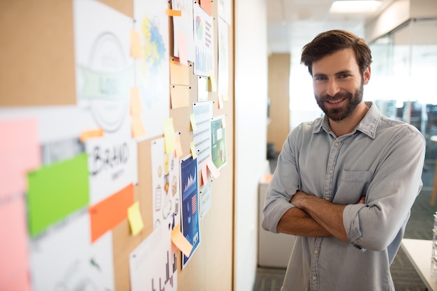 Smiling businessman with arms crossed standing by charts