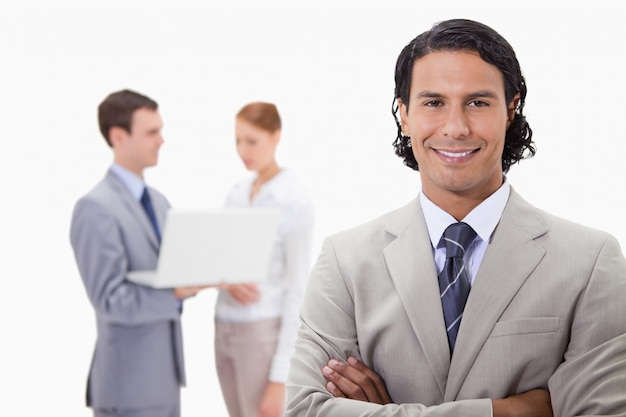 Smiling businessman with colleagues working on laptop behind him