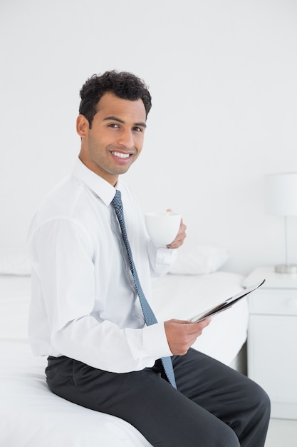 Smiling businessman with cup reading newspaper at hotel room