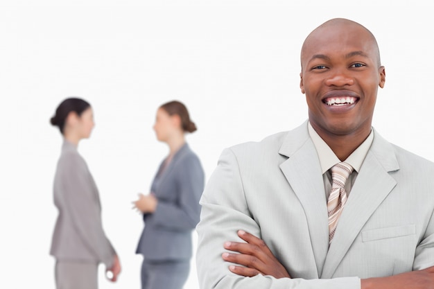 Smiling businessman with folded arms and co-workers behind him