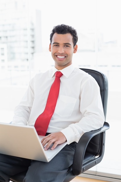 Smiling businessman with laptop sitting at office