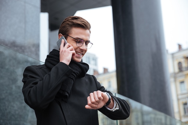 Smiling Businessman with phone in the street. man looking at wristwatch