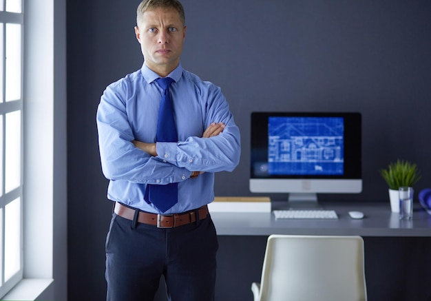 Smiling businessman with touchpad standing at workplace in office