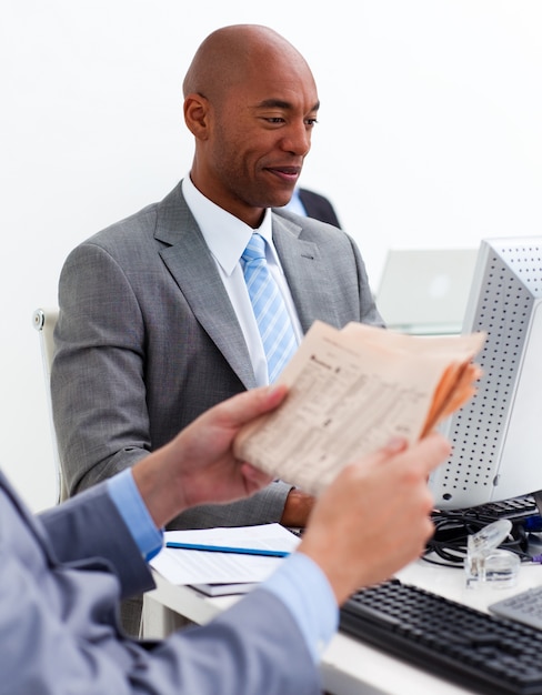 Smiling businessman working at a computer with his colleague reading a newspaper