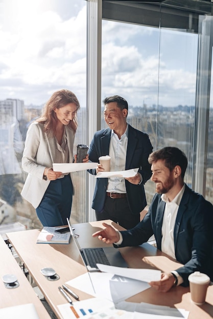 Photo smiling businessmen drink coffee and discussing documents with graphs and charts