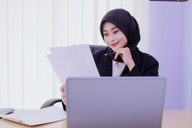 Smiling businesswoman analyzing document sitting in the office