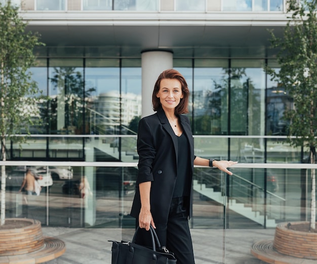 Smiling businesswoman in black formal wear holding a bag