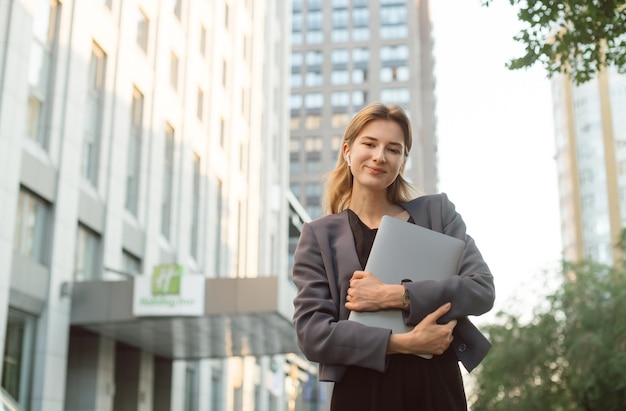 Smiling businesswoman carry laptop using wireless headphones outdoor modern city urban life concept