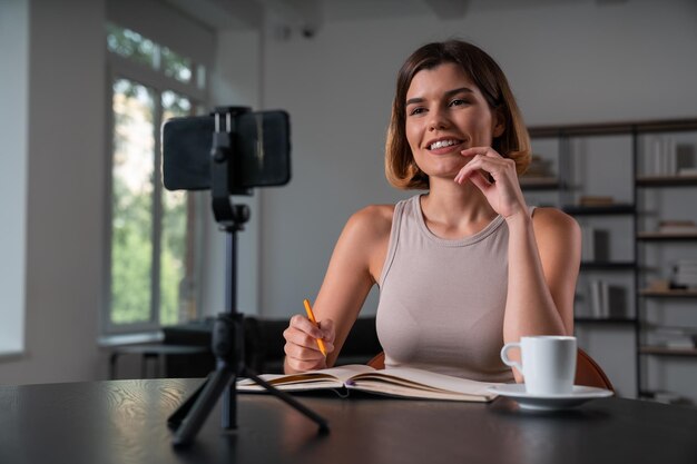 Smiling businesswoman in casual wear making video blog using
smartphone