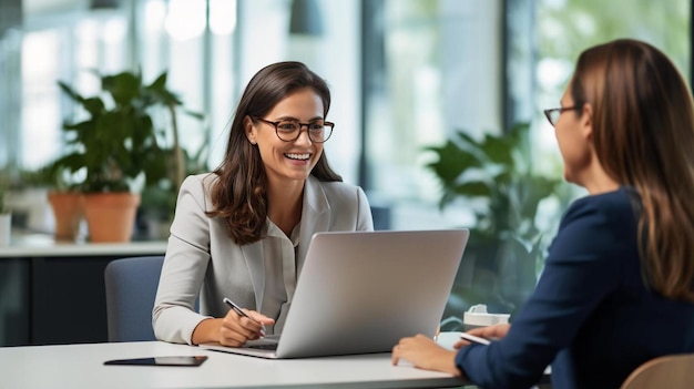 smiling businesswoman discussing with colleague over laptop at desk in office