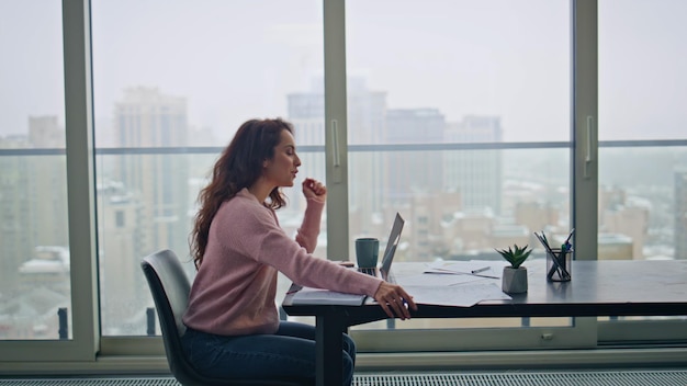 smiling businesswoman greeting laptop videocall talking at remote office table