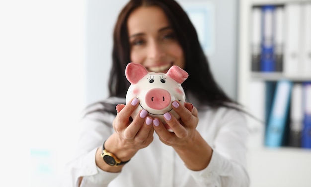 Smiling businesswoman holding white pink piggy bank