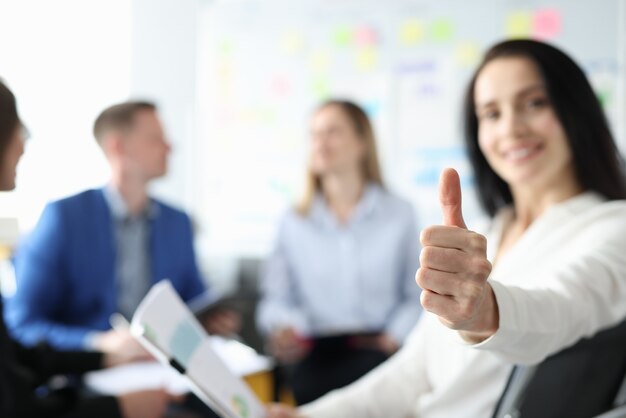 Smiling businesswoman holds thumbs up behind her team of businessmen