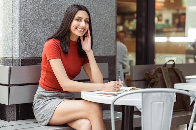 Smiling businesswoman looking at camera taking notes in cafe