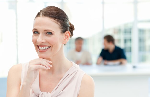 Smiling businesswoman looking at the camera while her coworkers are talking