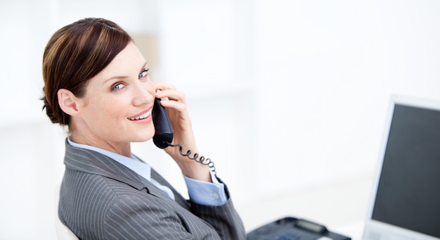 Photo smiling businesswoman on phone sitting at her desk