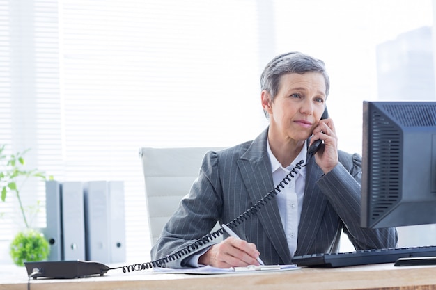 Smiling businesswoman phoning and writing at the office 