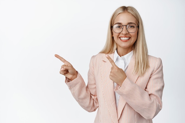 Smiling businesswoman pointing fingers left and showing advertisement demonstrating promo or chart diagram to the left standing over white background