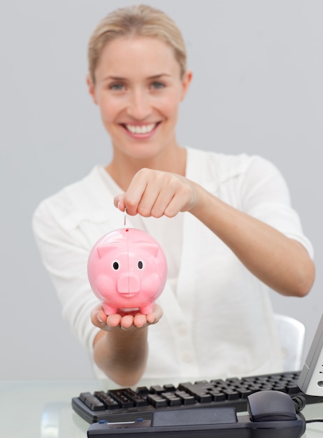 Donna di affari sorridente che risparmia soldi in un piggibank