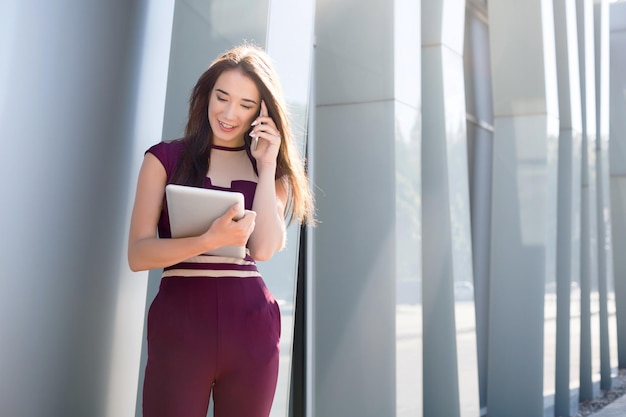 모바일 및 작업 태블릿에 얘기 웃는 사업가. 장치를 보고 스마트폰으로 컨설팅하는 여성, 현대적인 사무실 센터 근처에 서서 공간 복사