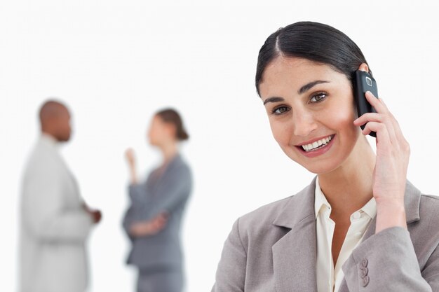 Smiling businesswoman with cellphone and co-workers behind her