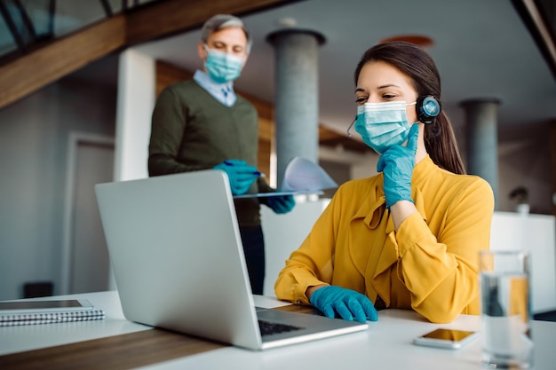 Smiling businesswoman with face mask making video call over laptop while working in the office