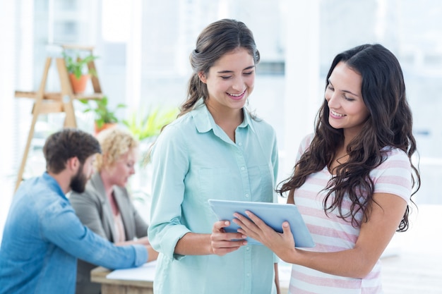 Smiling businesswomen using a tablet with colleagues