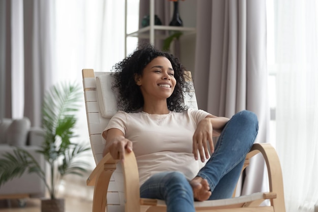 Photo smiling calm young black woman relaxing on comfortable wooden rocking chair in living room happy healthy black girl enjoy breathing fresh air resting in armchair at home feel stress free on weekend