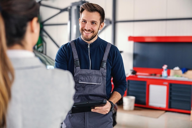 Smiling car seller talking to a mechanic and showing okay hand gesture while standing in car salon