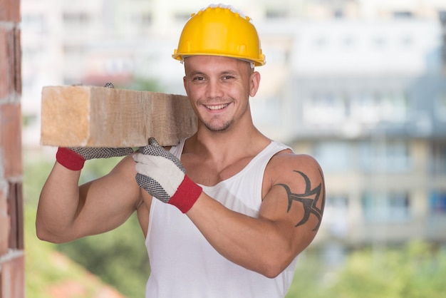 Smiling Carpenter Carrying A Large Wood Plank On His Shoulder