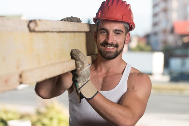 Foto falegname sorridente che porta una grande tavola di legno sulla sua spalla