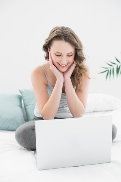 Smiling casual brunette looking at laptop in bed