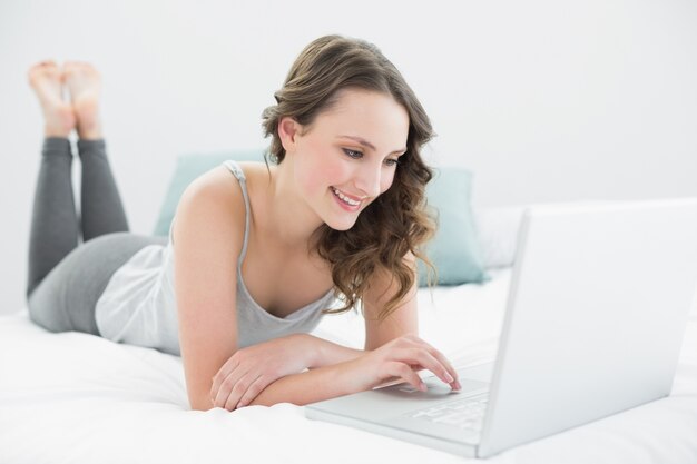 Photo smiling casual brunette using laptop in bed