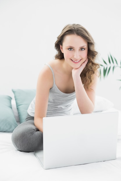 Smiling casual brunette using laptop in bed